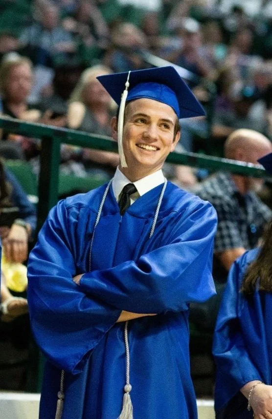 student smiling with his arms crossed at graduation